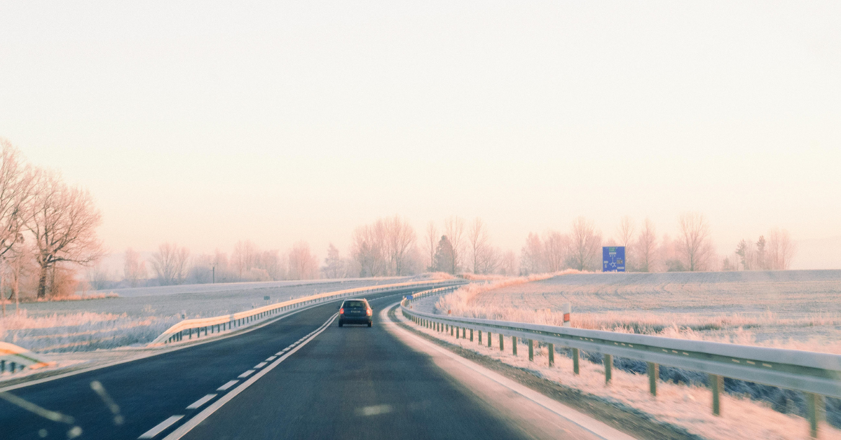 A car on a winter PCS driving down a highway with frosty guardrails and snowy fields visible in the background.