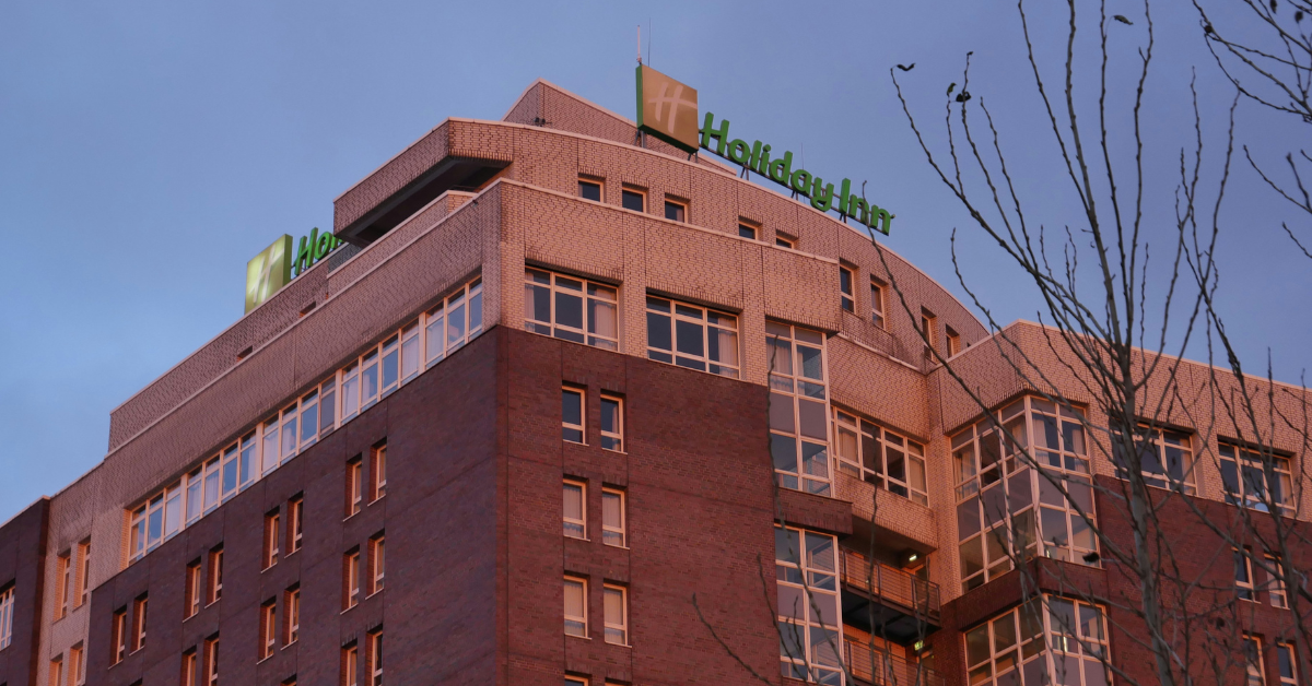 A multi-story Holiday Inn with red brick exterior and a tree in the foreground, representing the IHG Hotels and Resorts brand coming to Air Force on-base lodging through the DAF commercial lodging partnership.